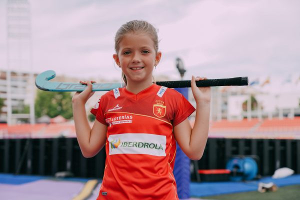 niña con el palo de hockey posado en los hombros lleva camiseta femenina de la selección española de hockey hierba