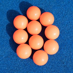 10 bolas o pelotas naranjas de hockey hierba sobre el campo de césped artificial azul