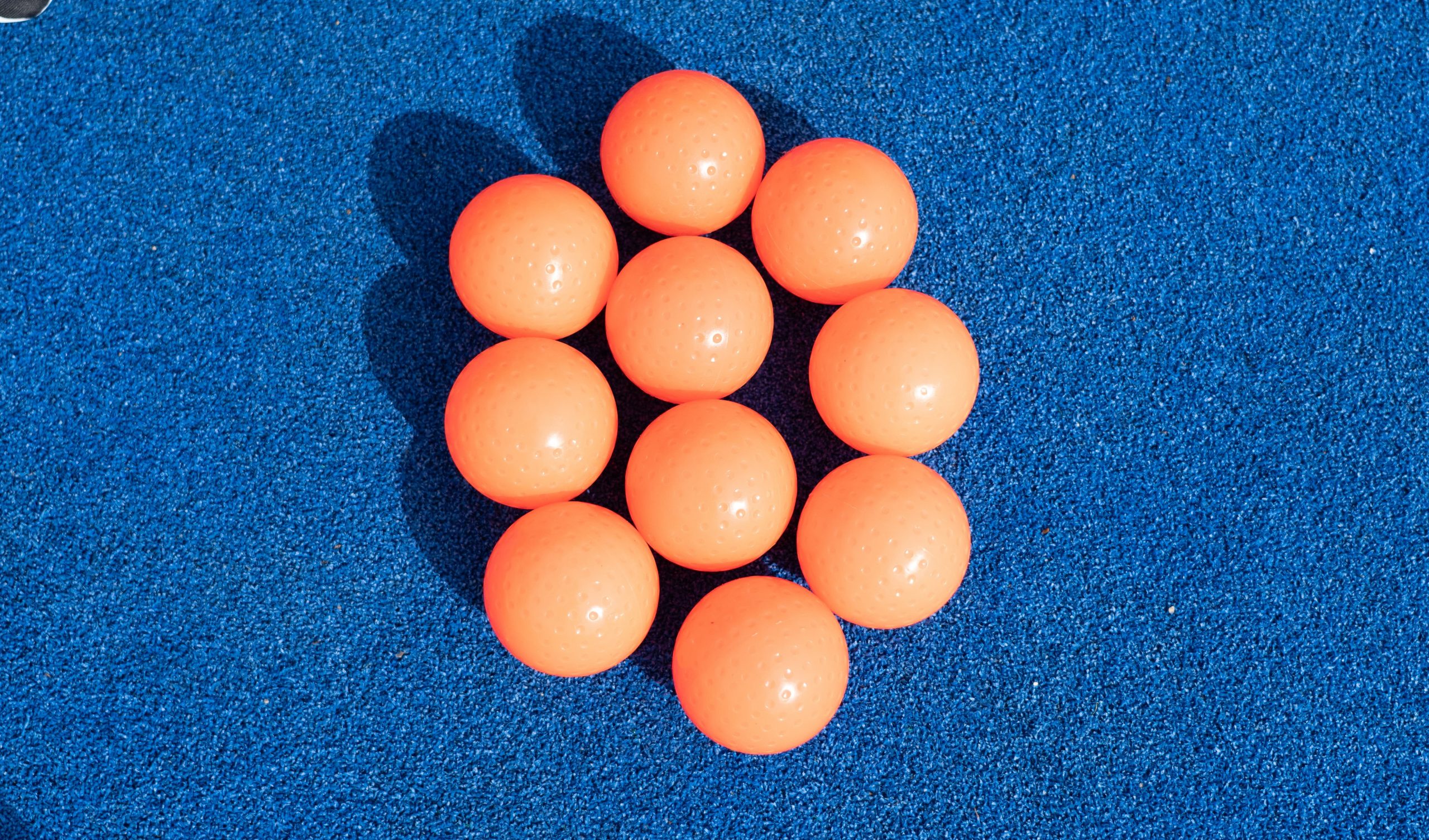 10 bolas o pelotas naranjas de hockey hierba sobre el campo de césped artificial azul